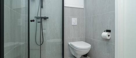 A bathroom with a glass-enclosed shower, a toilet, and a wall-mounted toilet paper holder.