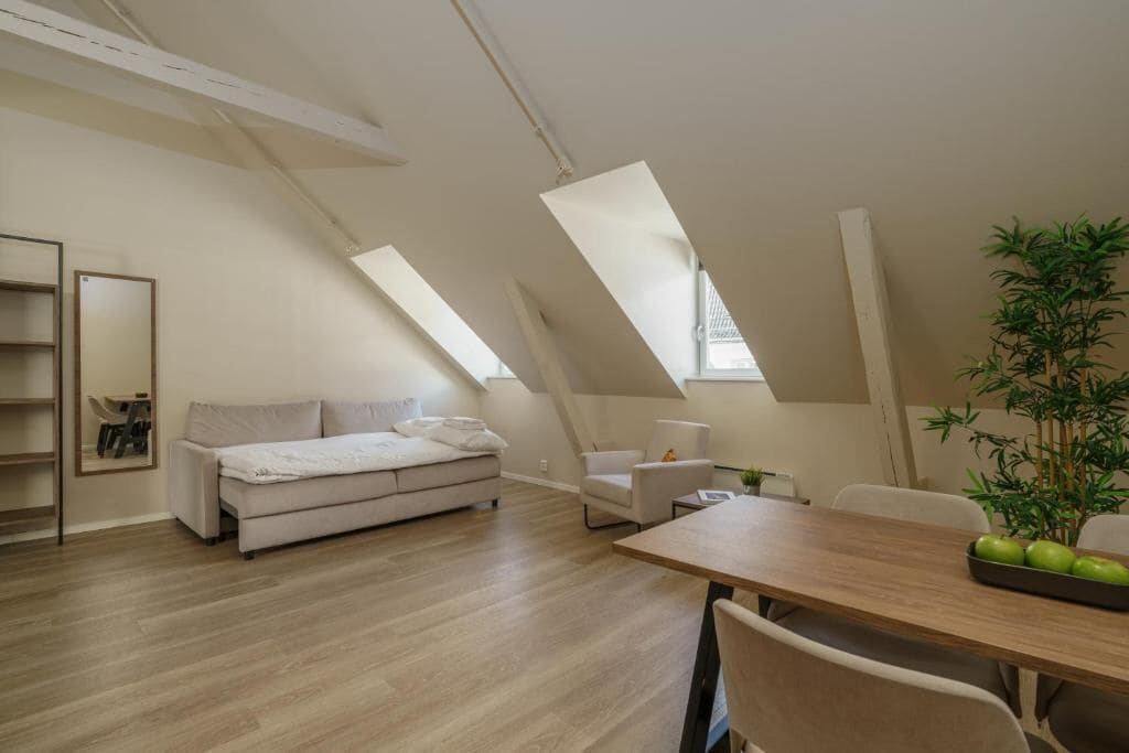A modern loft bedroom with a sloped ceiling, a sofa, a dining table, and a potted plant.