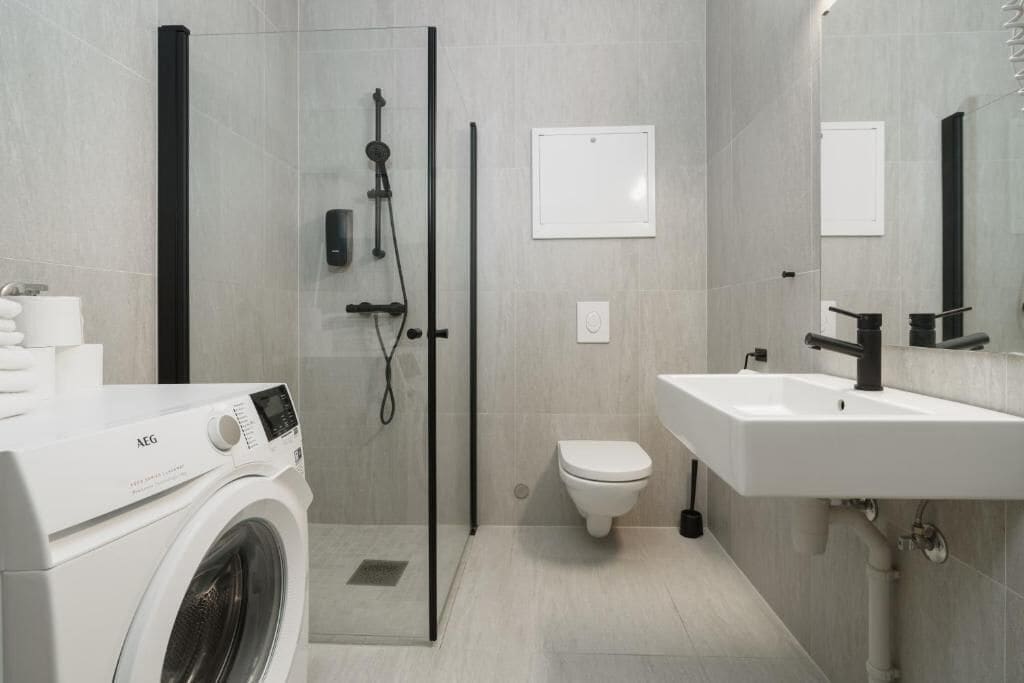 Ein modernes Badezimmer mit Waschmaschine, Duschkabine aus Glas, Toilette und Waschbecken.
