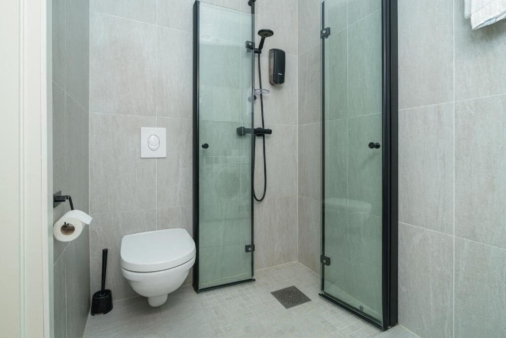 Ein modernes Badezimmer mit einer gläsernen Duschkabine, einer Toilette und einem Handtrockner.