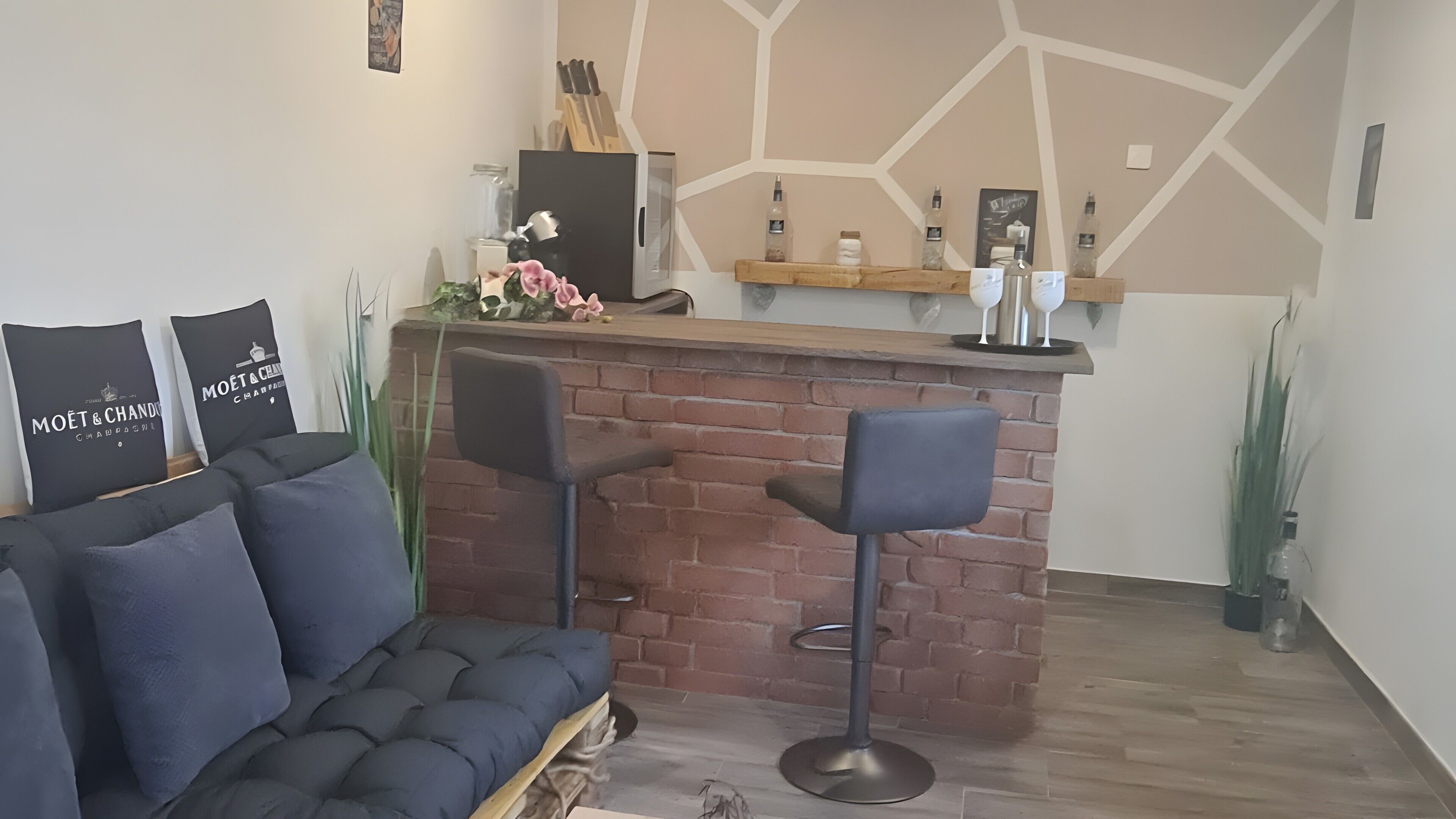 Uma sala de estar moderna com parede de destaque em tijolo, um sofá preto, dois banquetes e um balcão de bar em madeira.