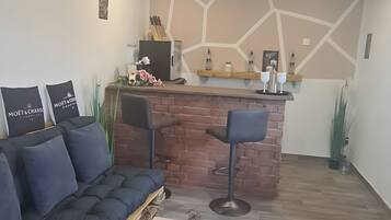 Uma sala de estar moderna com parede de destaque em tijolo, um sofá preto, dois banquetes e um balcão de bar em madeira.
