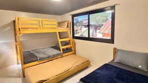 A room with a bunk bed, a single bed, a window with a view, and a ceiling light. - Balay Tori & Gil (Baguio)