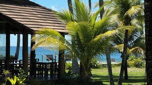 A wooden structure with a tiled roof, surrounded by palm trees and a view of the ocean. - Beachfront Apartment on the Upper Floor: Best Value for Money (Maraú)