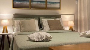 A hotel room with a bed, two bedside lamps, a wall-mounted air conditioner, and three framed pictures of the ocean. - Beachfront Apartment on the Upper Floor: Best Value for Money (Maraú)