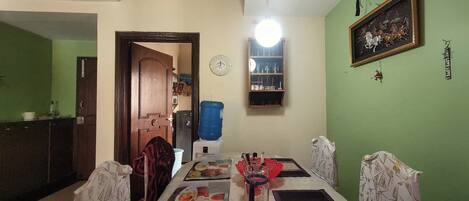 A dining area with a table set for two, chairs, a water dispenser, a clock, and a framed picture on the wall.
