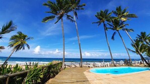 Une terrasse en bois qui mène à une piscine, avec des palmiers et une vue sur la plage.