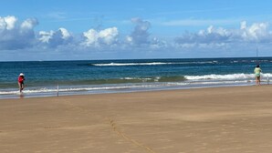 Une plage où deux personnes pêchent, un ciel dégagé et un bateau à l’horizon.