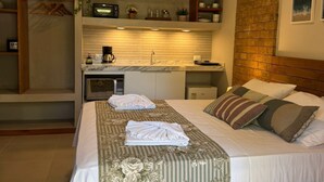 Une chambre d’hôtel avec un lit, une petite kitchenette, un mur décoratif en briques et un climatiseur fixé au plafond.