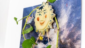 A decorative piece with a sun face, a bee, and green leaves.