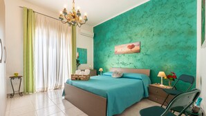 A bedroom with a bed, a chair, a nightstand, a lamp, a painting, and a window with curtains.