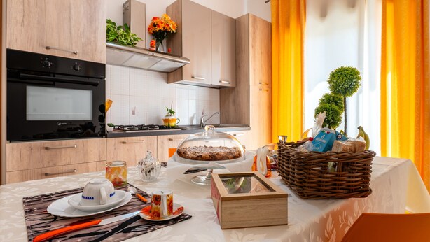 A modern kitchen with a built-in oven, a dining table set with a cake, and a basket of bread.