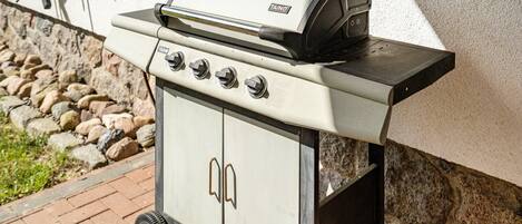 A portable gas grill with four burners and a digital display, mounted on a wheeled cart.