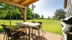 An outdoor patio with a table and chairs, a grill, and a view of a grassy area.