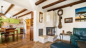 A cozy living room with a fireplace, wooden beams, and a dining area with green cabinets.