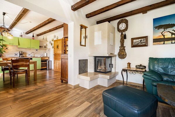 Una sala de estar acogedora con chimenea, vigas de madera y una zona de comedor con armarios verdes.