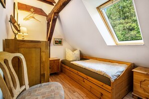 Un dormitorio con una cama de madera, una mesita de noche, un aparador, una silla, un espejo, una ventana con vistas a árboles y una viga de techo de madera.