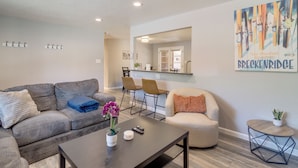 Una sala de estar moderna con sofá, sillón, mesa de centro y un cuadro en la pared.