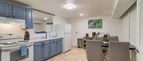 A kitchen with white appliances, blue cabinets, and a dining area with chairs and a table.
