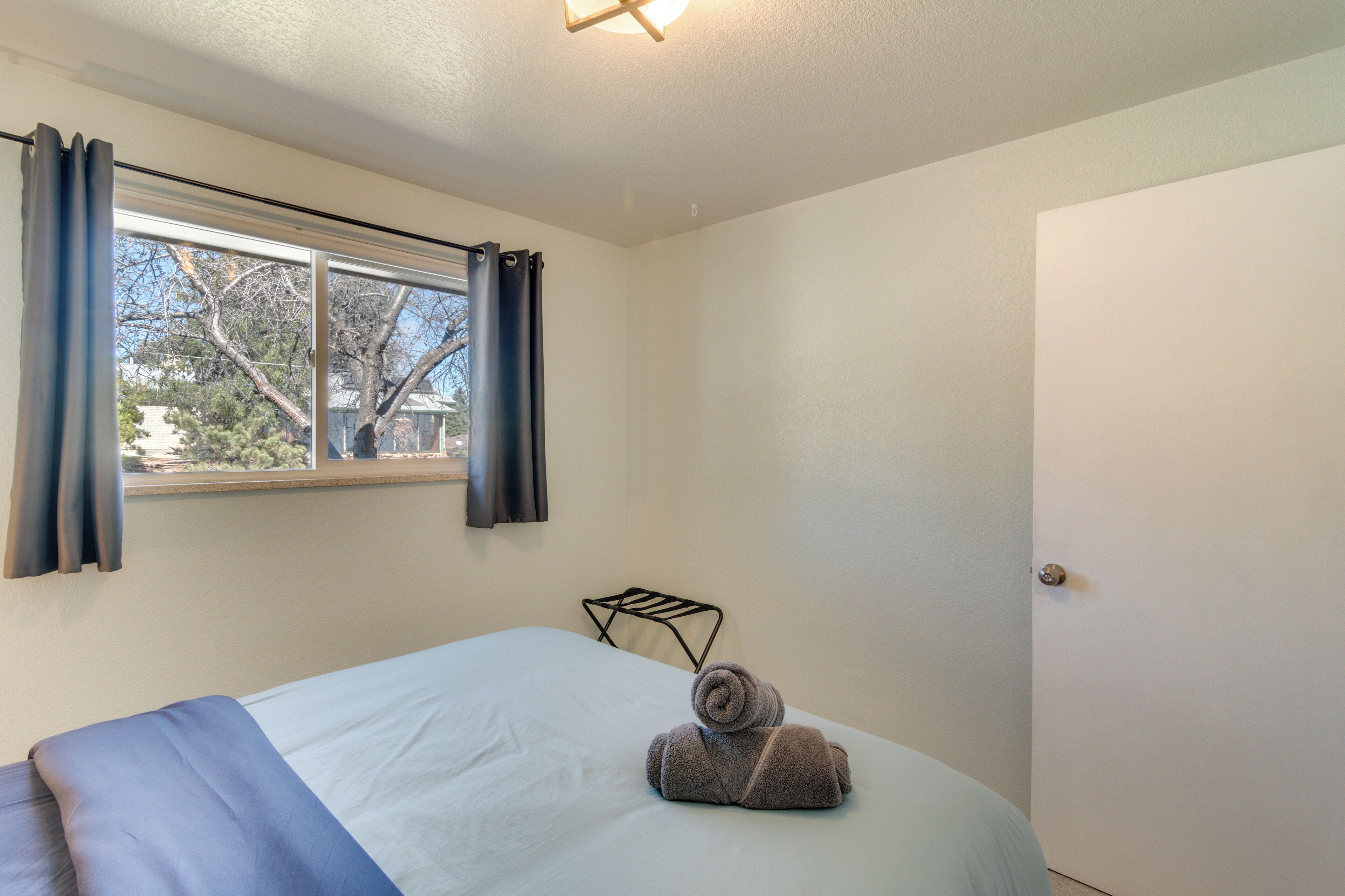 Habitación de hotel con cama, ventana con cortinas, una toalla sobre la cama y una puerta.