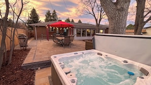 Un jacuzzi en un patio trasero con una sombrilla roja y una casa de ladrillo al fondo.