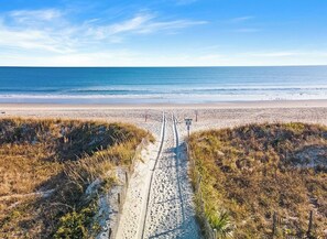 En stig som leder från stranden ut till havet, med ett staket och vägvisningsskyltar.