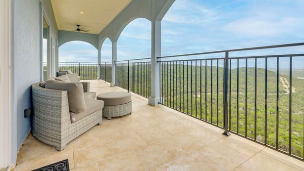 Un balcón techado con mobiliario exterior, vistas al paisaje y una barandilla.
