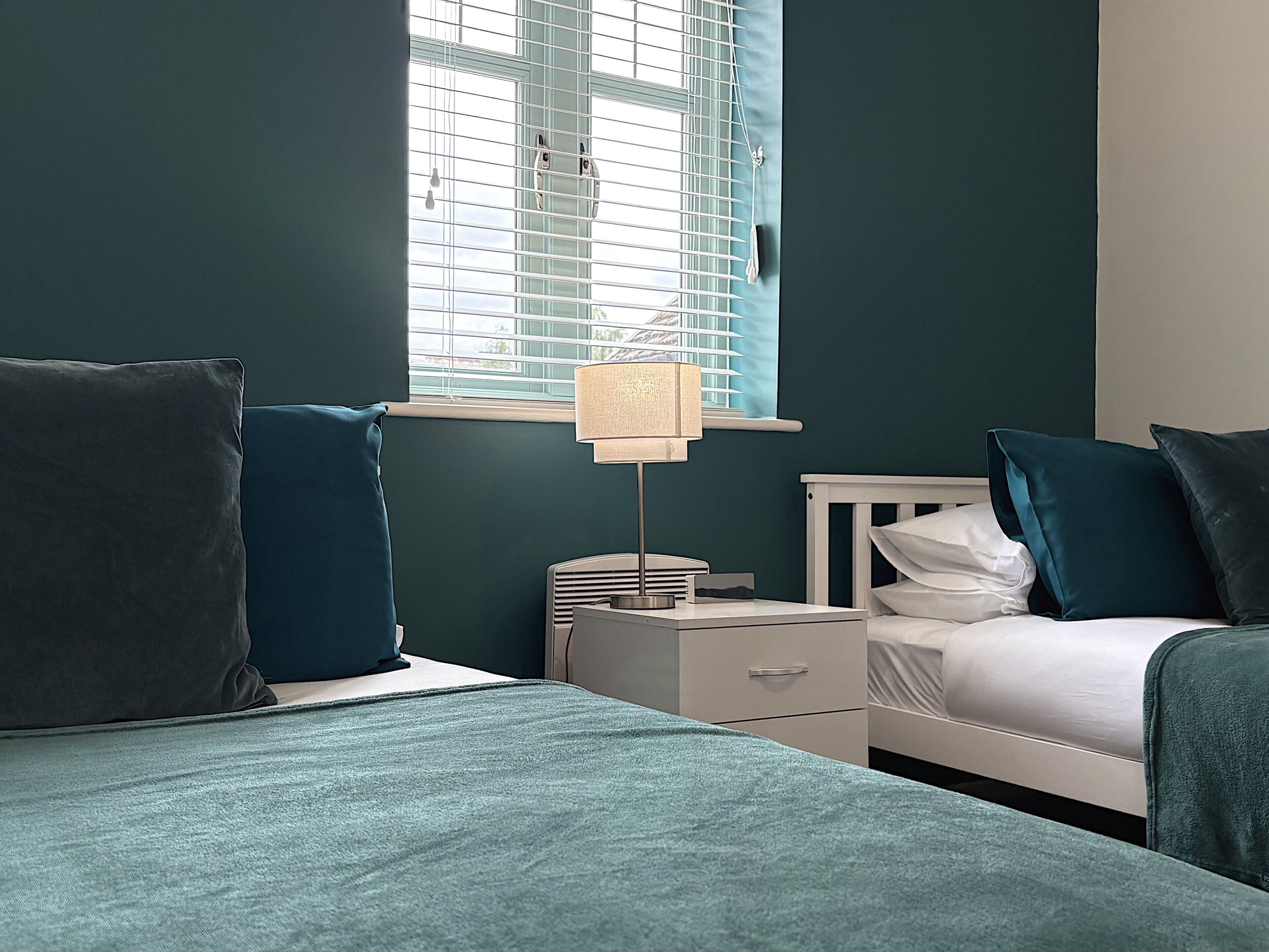 Una camera da letto con un letto, un comodino, una lampada e una finestra con persiane.