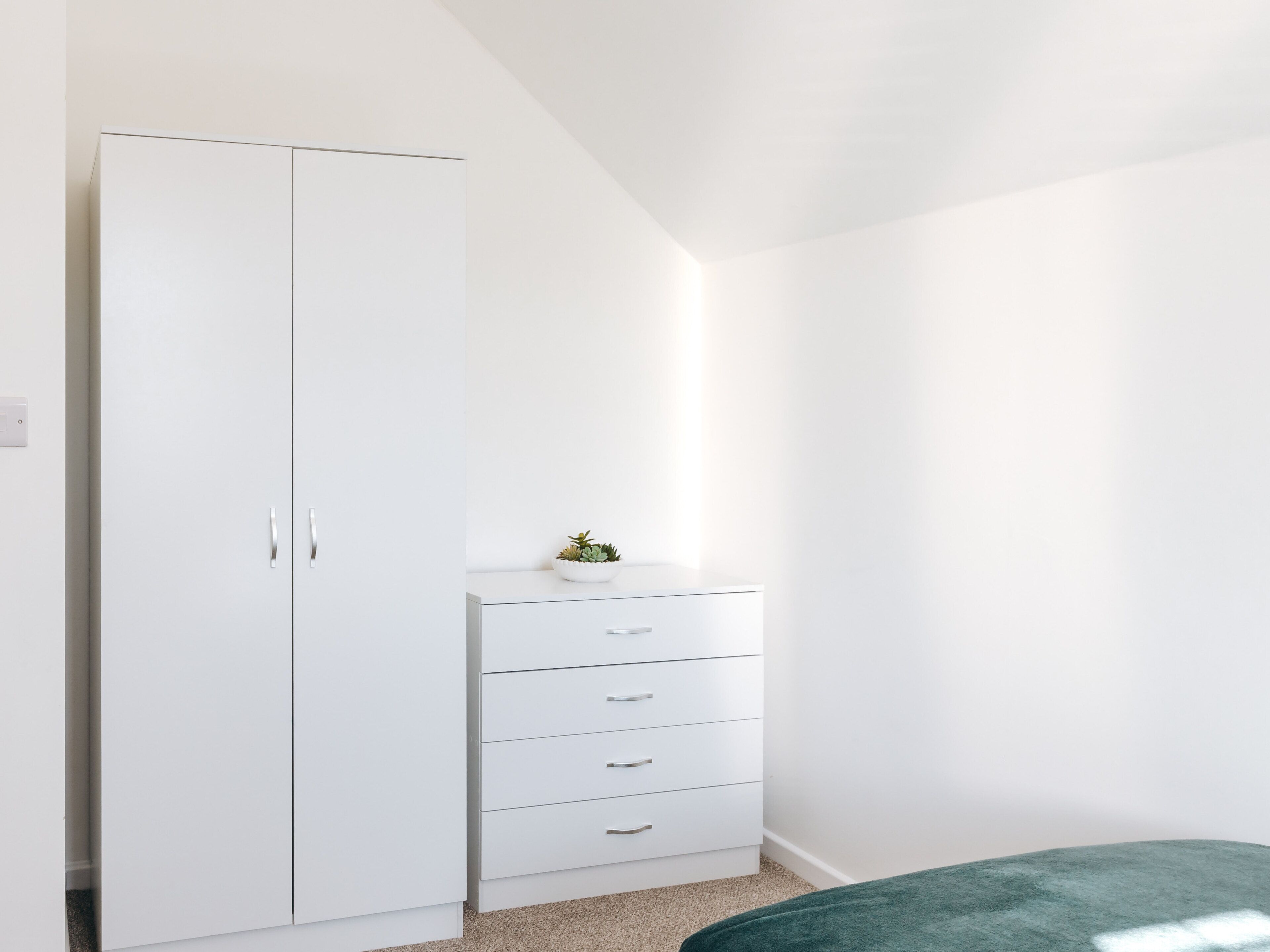 Una camera da letto con un armadio bianco, un piccolo comodino e una coperta verde.