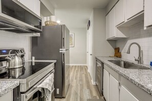 A modern kitchen with stainless steel appliances, a granite countertop, and a wooden floor. - Tiger Town Retreat: Spacious 3-home Retreat! (Baton Rouge)