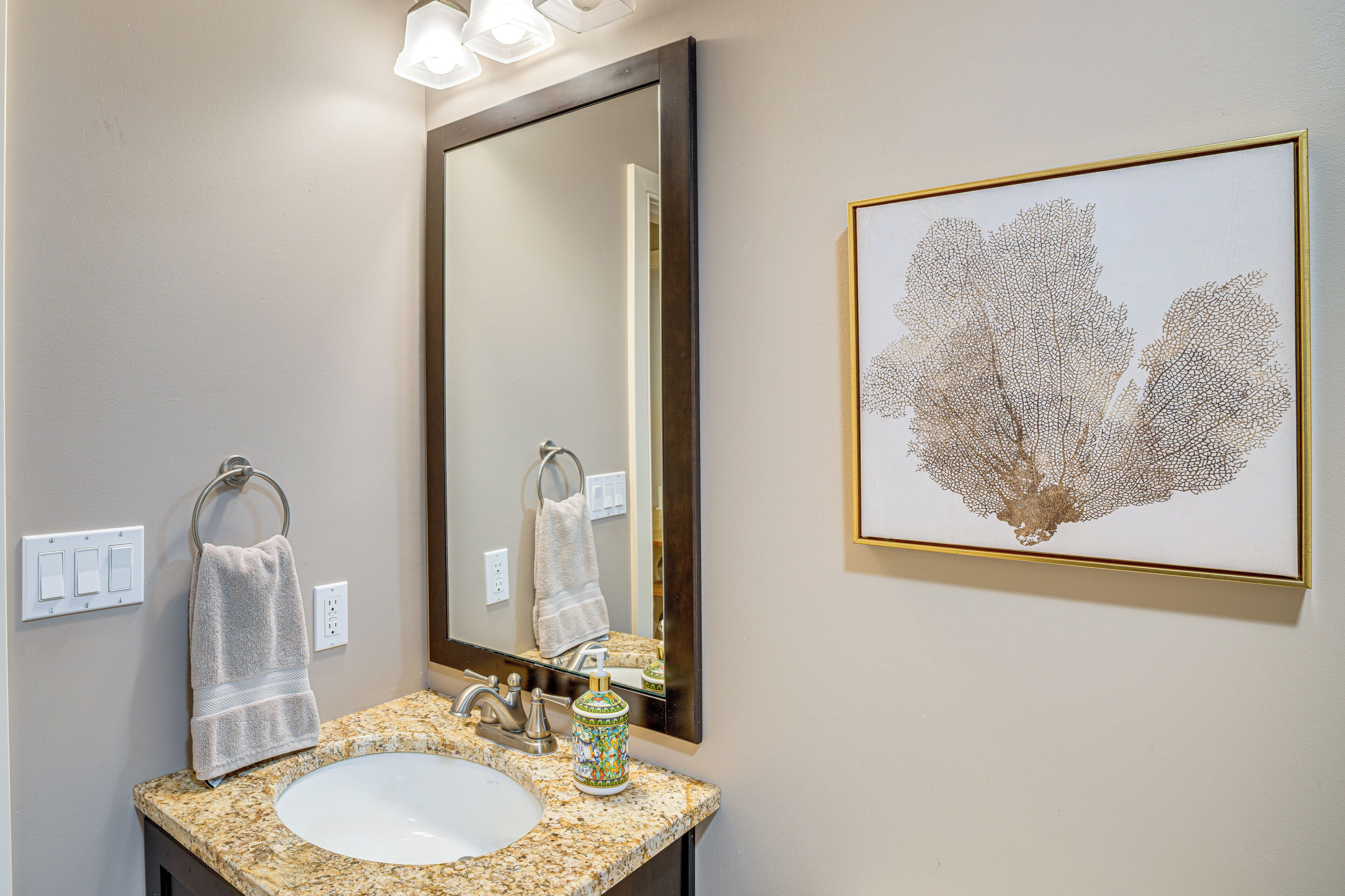 A bathroom with a granite countertop, a sink, a mirror, and a framed artwork on the wall.