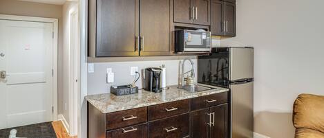 A compact kitchen with dark wood cabinets, a built-in microwave, a stainless steel refrigerator, and a coffee maker on the counter.