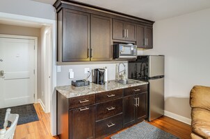 Una cocina compacta con armarios de madera oscura, un microondas integrado, un refrigerador de acero inoxidable y una cafetera sobre la encimera.