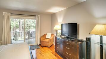 A hotel room with a bed, a TV, a dresser, a chair, and a balcony with a view of trees.