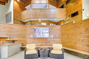 A wooden interior with a high ceiling, a central seating area with two chairs, a table, and a ski-themed artwork on the wall. - Seven Springs Escape! 2 Connected Ski-in/out Units (Champion)