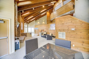 A spacious indoor area with a high ceiling, wooden beams, wicker furniture, and a stone wall. - Seven Springs Escape! 2 Connected Ski-in/out Units (Champion)