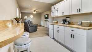 A kitchen with white cabinets, a wooden countertop, a ceiling fan, and a dining area with stools.