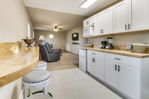 A kitchen with white cabinets, a wooden countertop, a ceiling fan, and a seating area with a chair and stools. - Fishermen's Oasis! Steps to Dtwn & White River (Cotter)