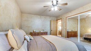 A bedroom with a large bed, a dresser, a mirror, and a ceiling fan.