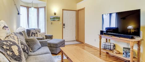 A living room with a sofa, ottoman, coffee table, television, and a door.