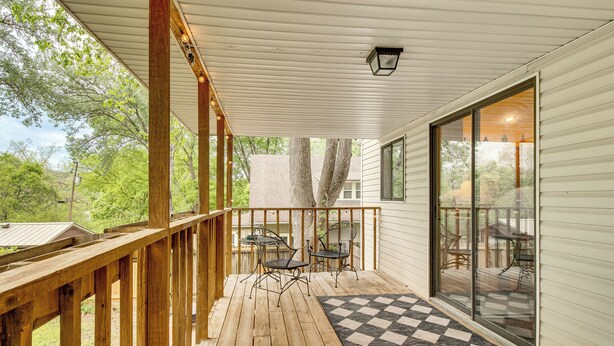 A wooden deck with a checkered rug, metal chairs, and a glass door leading to an outdoor area.