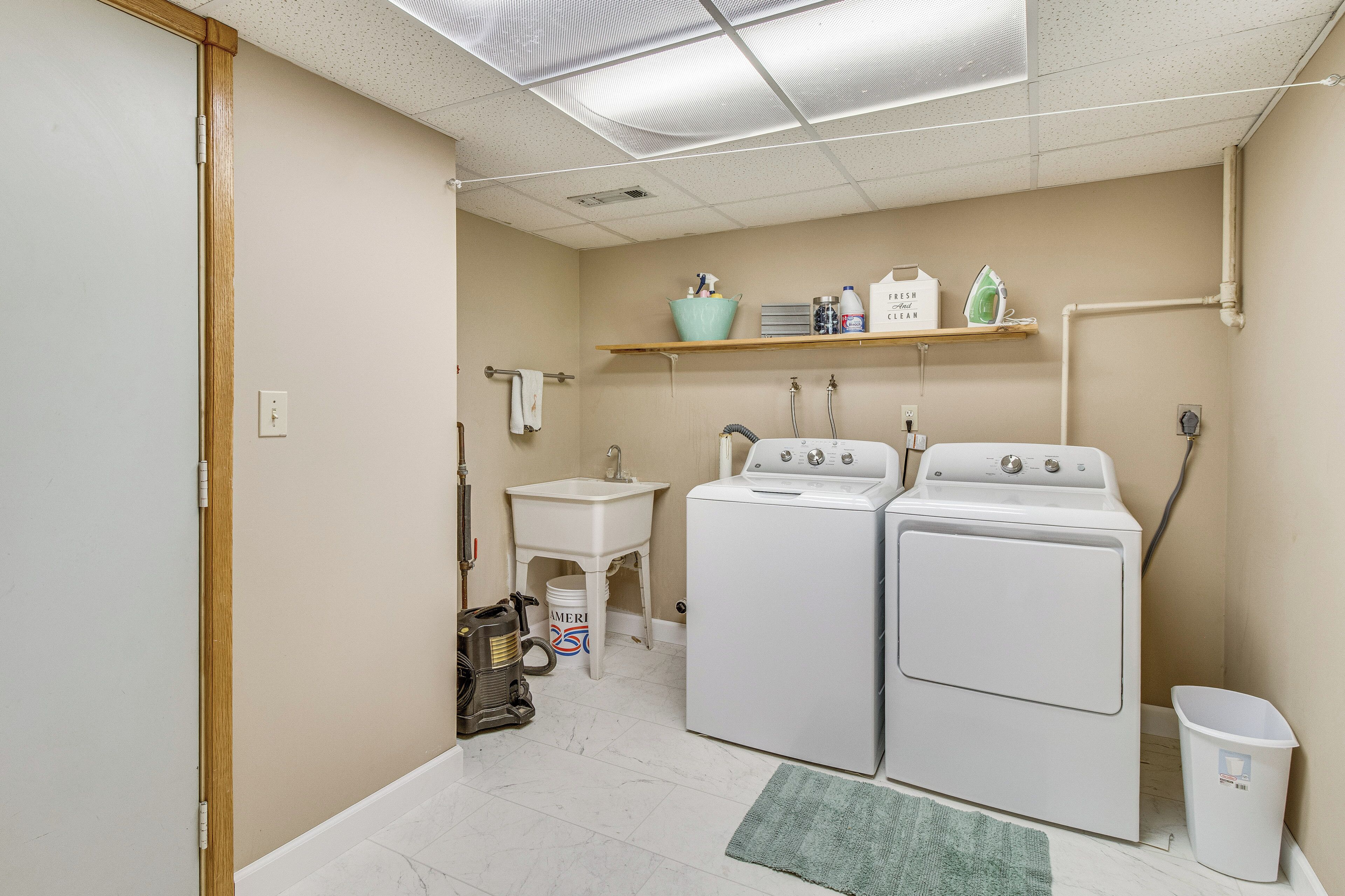 A laundry room with two washers and dryers, a sink, and a shelf with cleaning supplies.