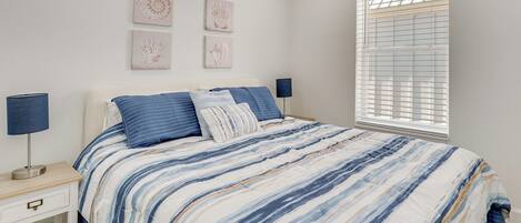 A bedroom with a bed, bedside tables, wall art, and a window with blinds.