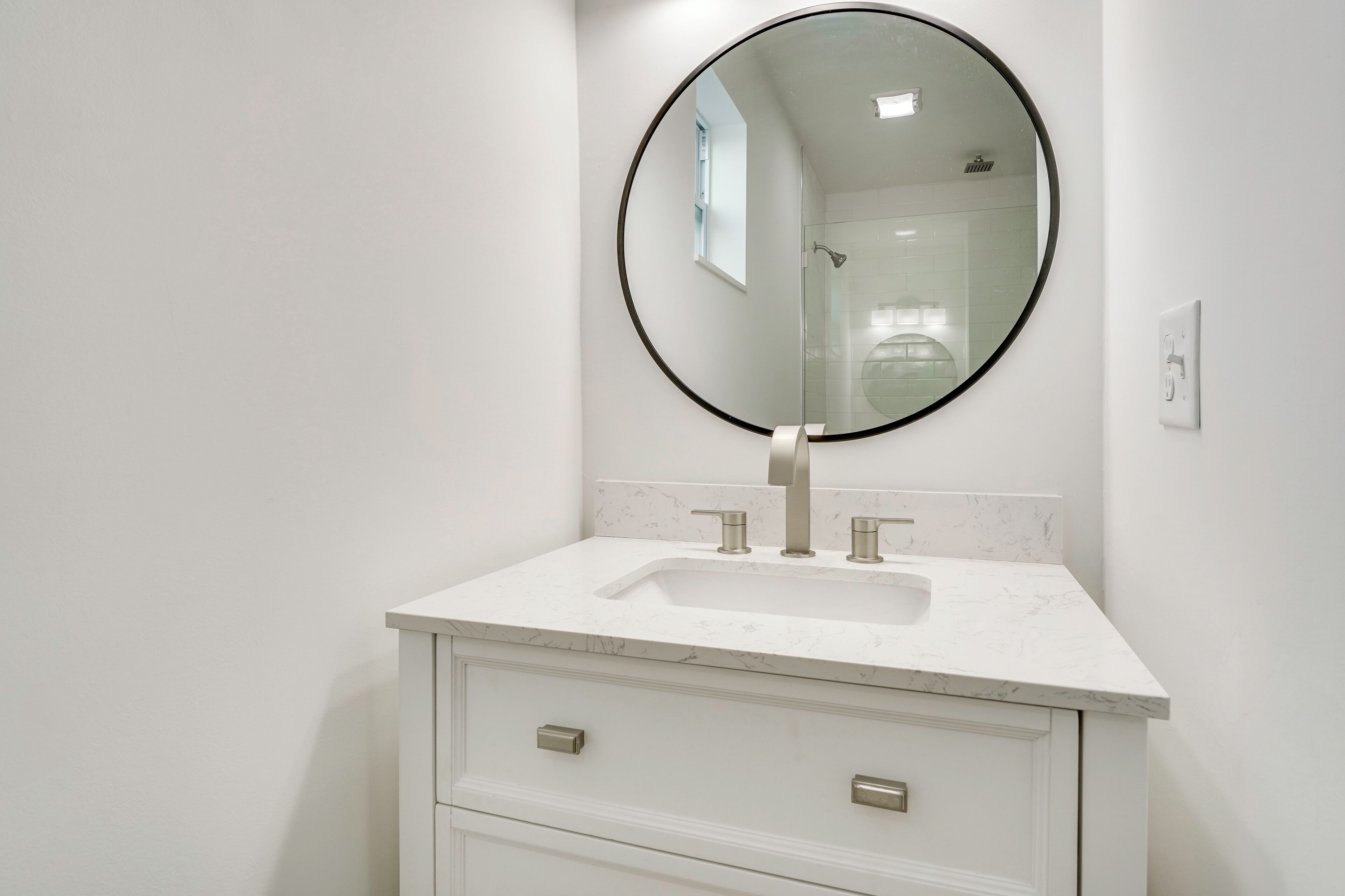 Een badkamer met een wit wastafelmeubel, een ronde spiegel en een douchecabine met glazen wanden.