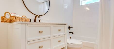 A bathroom with a white vanity, a round mirror, a toilet, and a shower area.