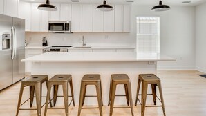 Una cocina moderna con armarios blancos, un refrigerador de acero inoxidable, un microondas y una isla grande con taburetes.
