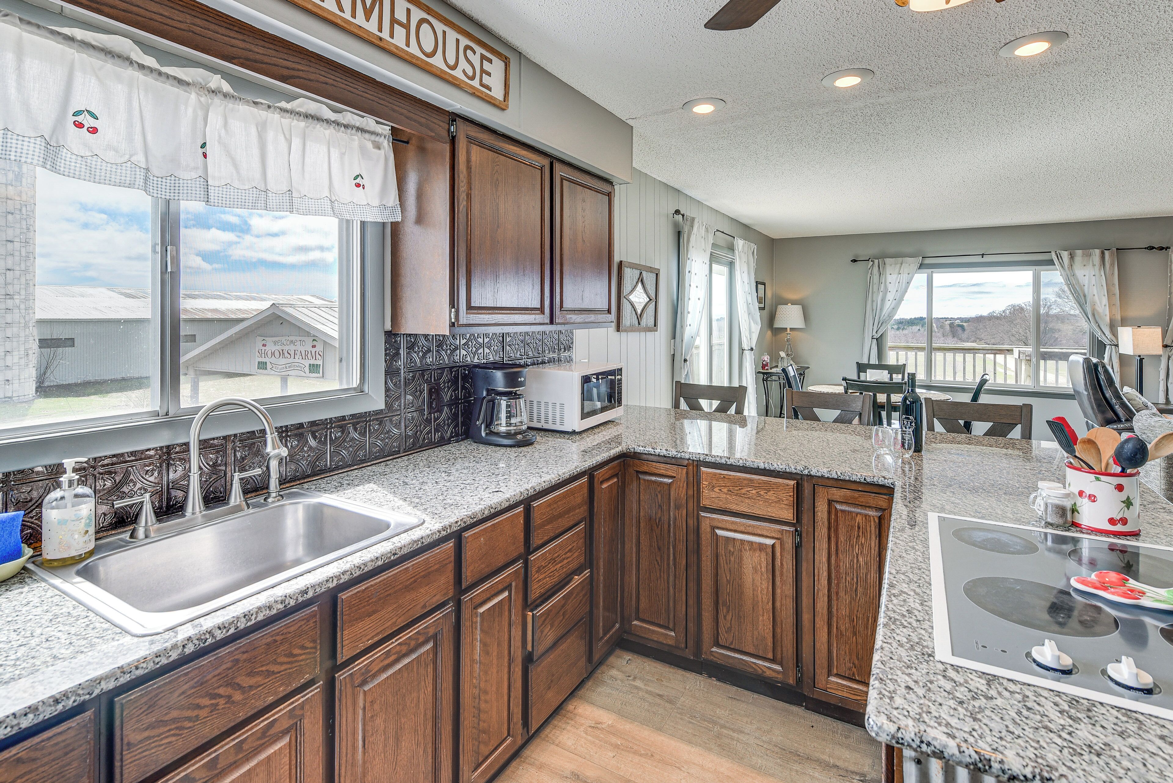 A kitchen with wooden cabinets, a granite countertop, a sink, and a view of a house outside.