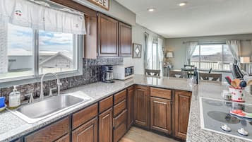 A kitchen with wooden cabinets, a granite countertop, a sink, and a view of a house outside.