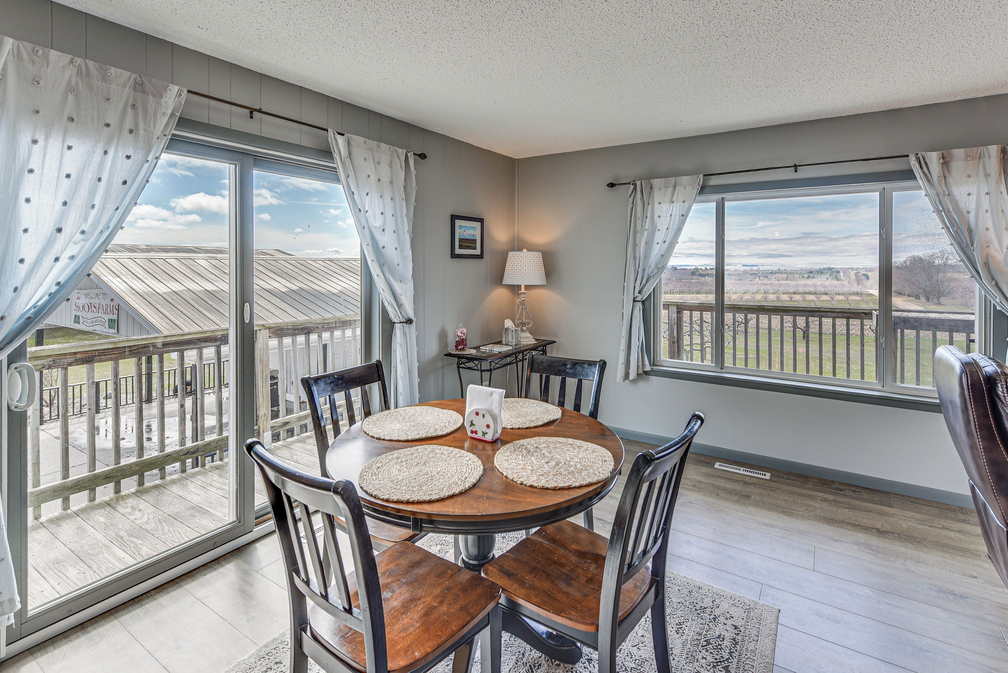 A dining area with a round table, chairs, and a view through large windows.