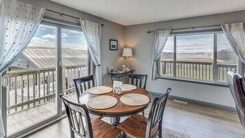 A dining area with a round table, chairs, and a view through large windows.